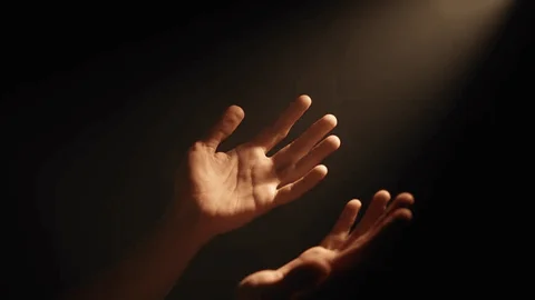 Hands lifted in prayer under a beam of light